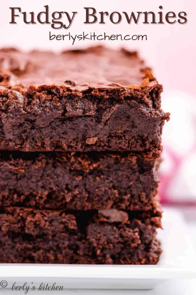 Three fudgy brownies stacked on a plate.
