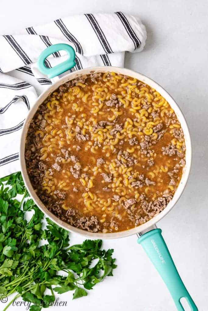 Beef broth and elbow macaroni added to the pan.