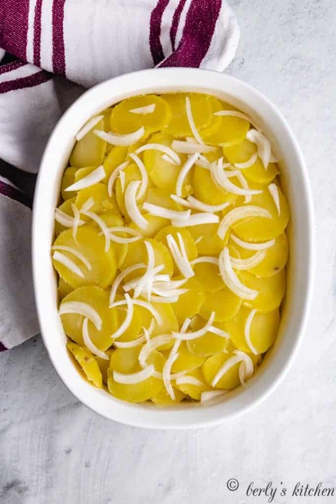 Sliced potatoes and onions in a casserole dish.