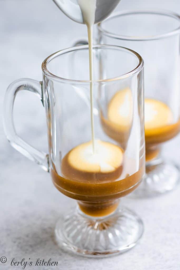 Heavy cream being poured into a mug of butterscotch sauce.