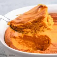 A scoop of carrot soufflé lifted from a baking dish.