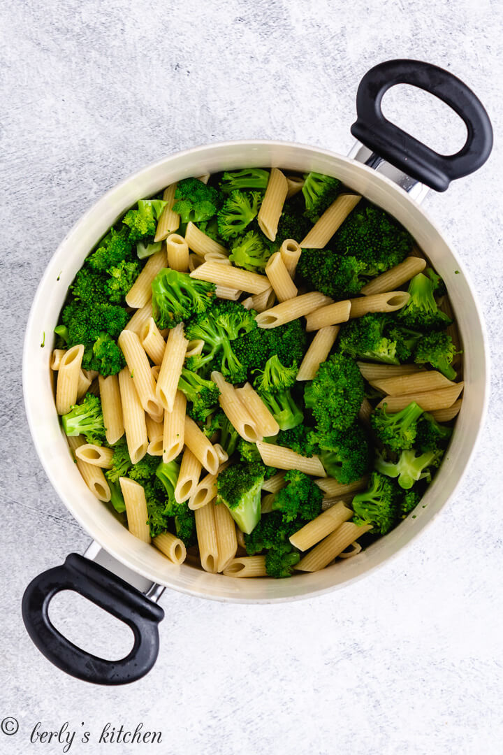 Penne noodles and broccoli florets cooked in a pot.