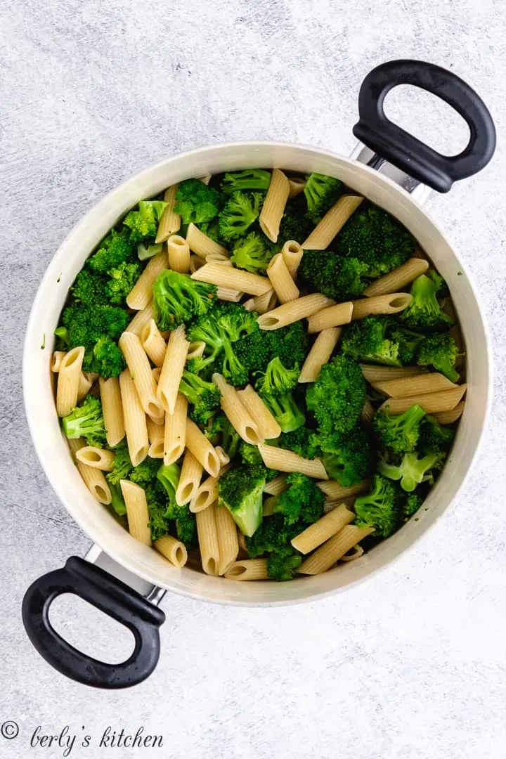 Penne noodles and broccoli florets cooked in a pot.