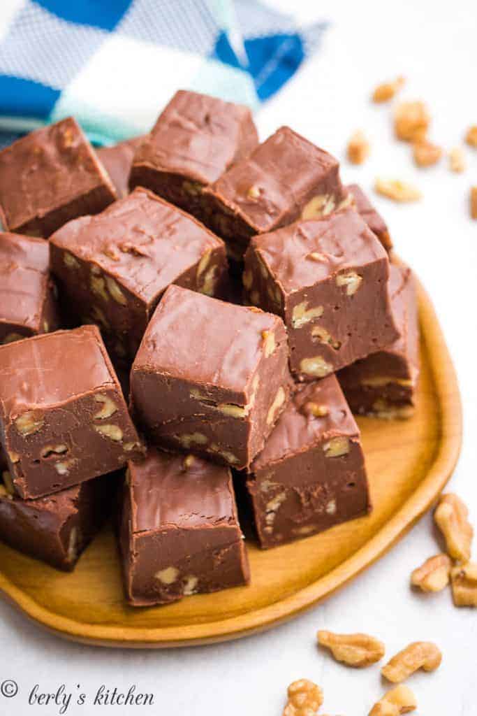 Squares of fudge stacked on a wooden plate.