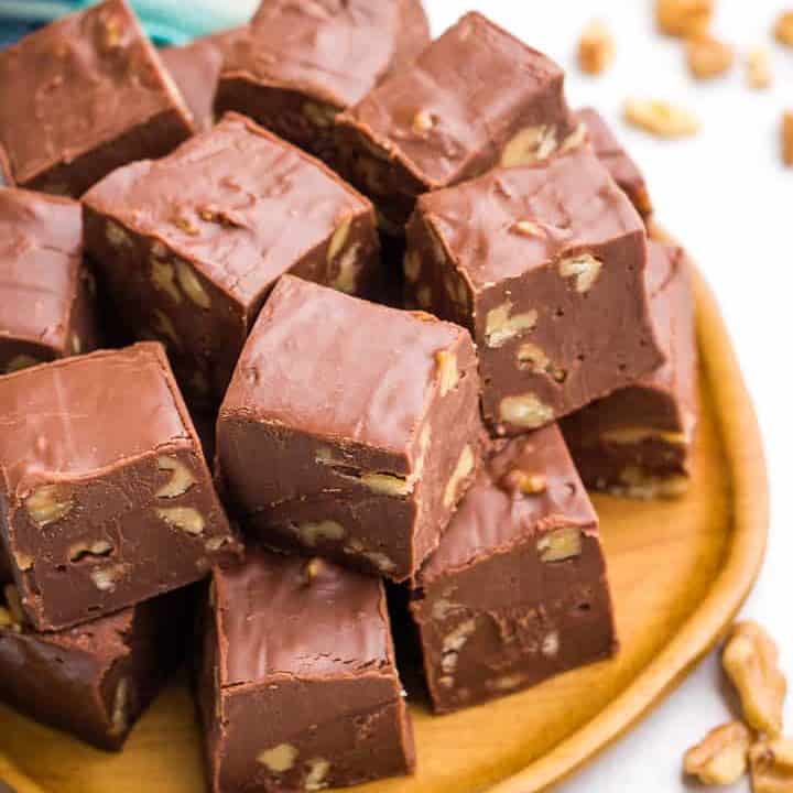 Squares of fudge stacked on a wooden plate.