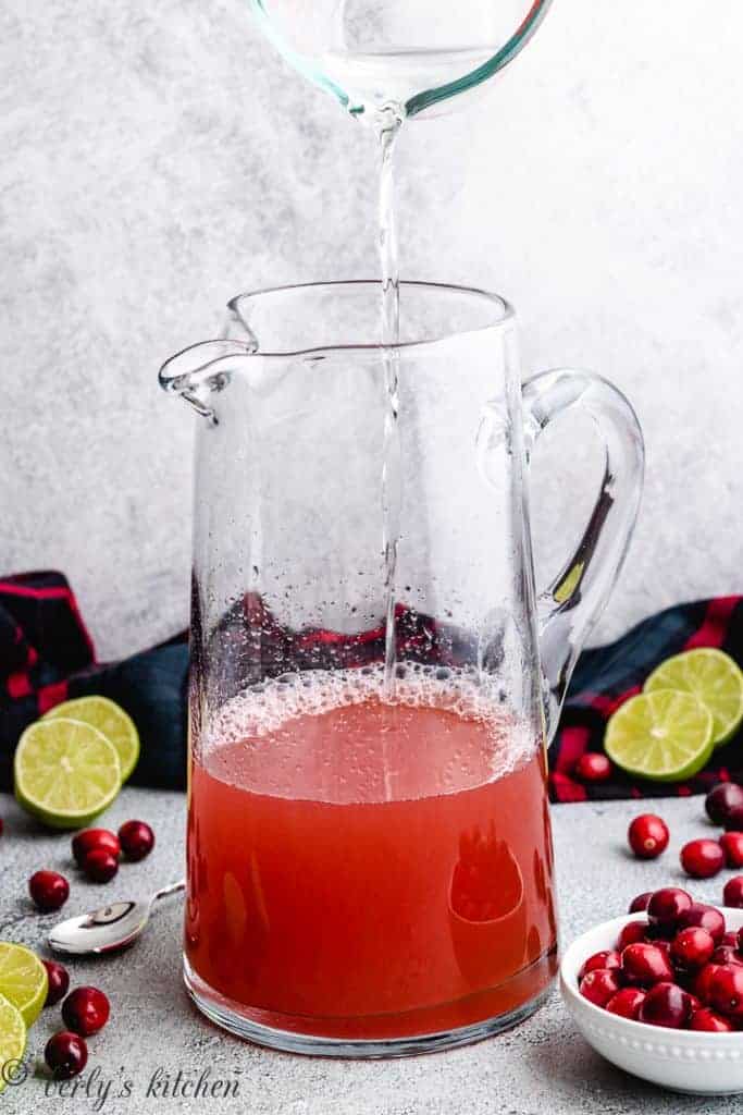 Tequila being added to the pitcher of juice.