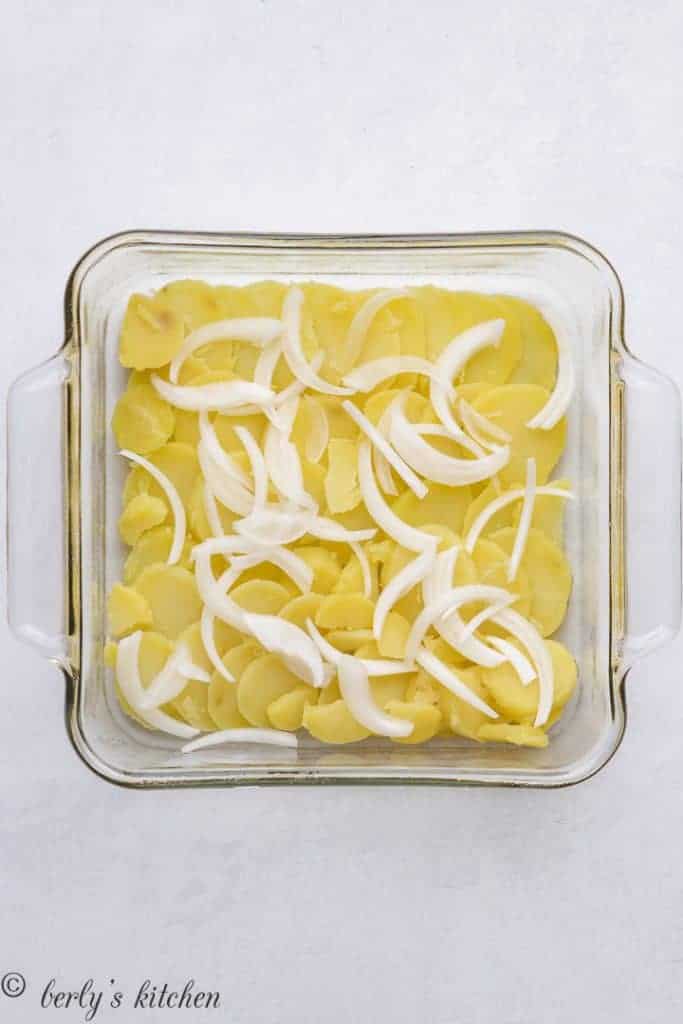 Sliced onions and boiled potatoes layered in a baking dish.