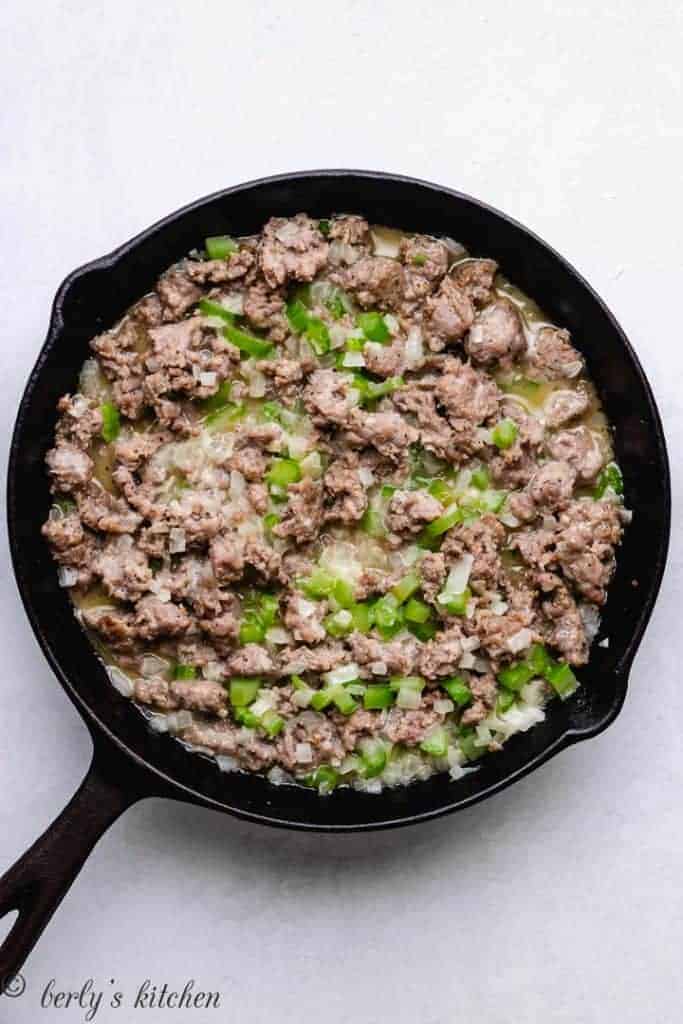 Sausage, onions, and other ingredients sautéing in a skillet.