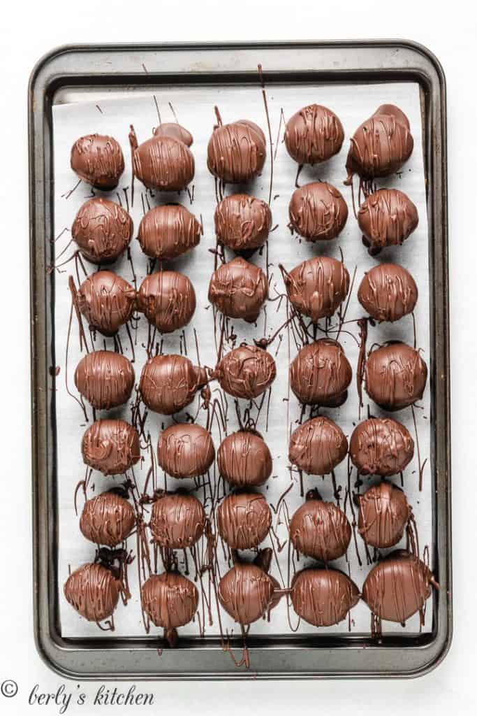 The dipped peanut butter balls placed on a lined baking sheet.