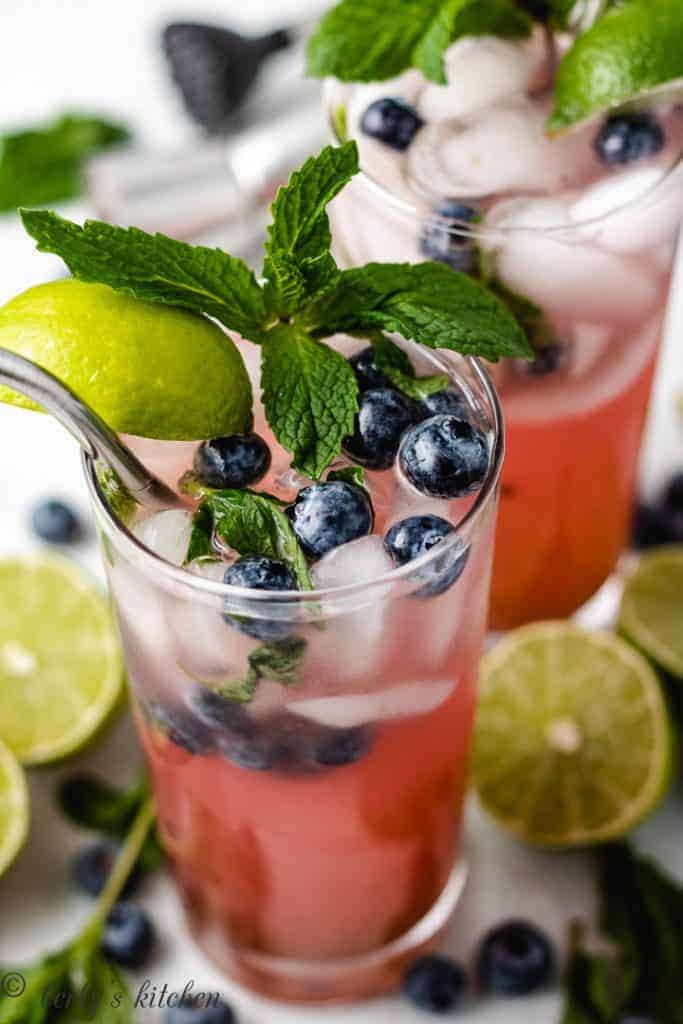 Two blueberry mojitos garnished with fresh berries and mint.