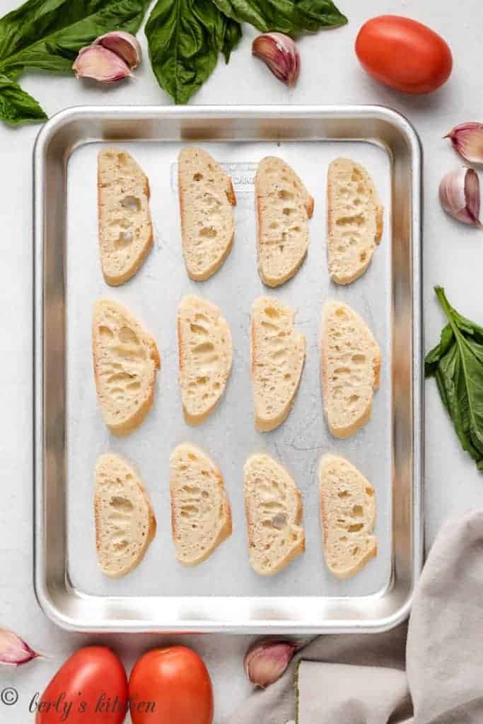 Slices of french baguette on a baking sheet.