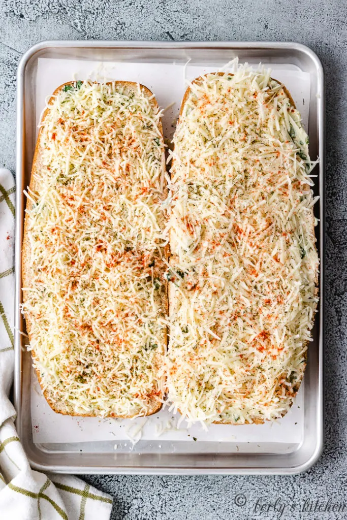 Two loaves of bread topped with shredded cheese.
