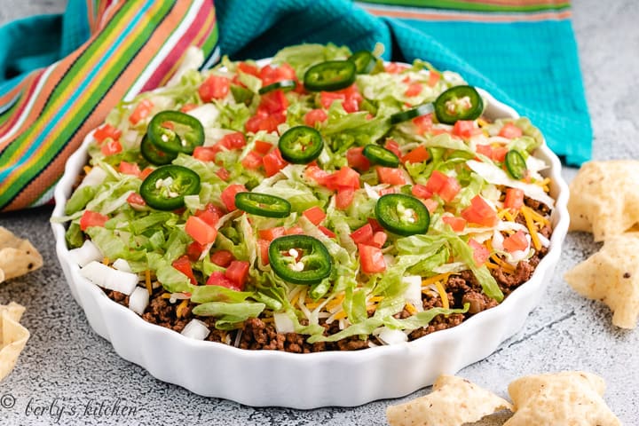 Taco dip in a white dish with taco toppings.