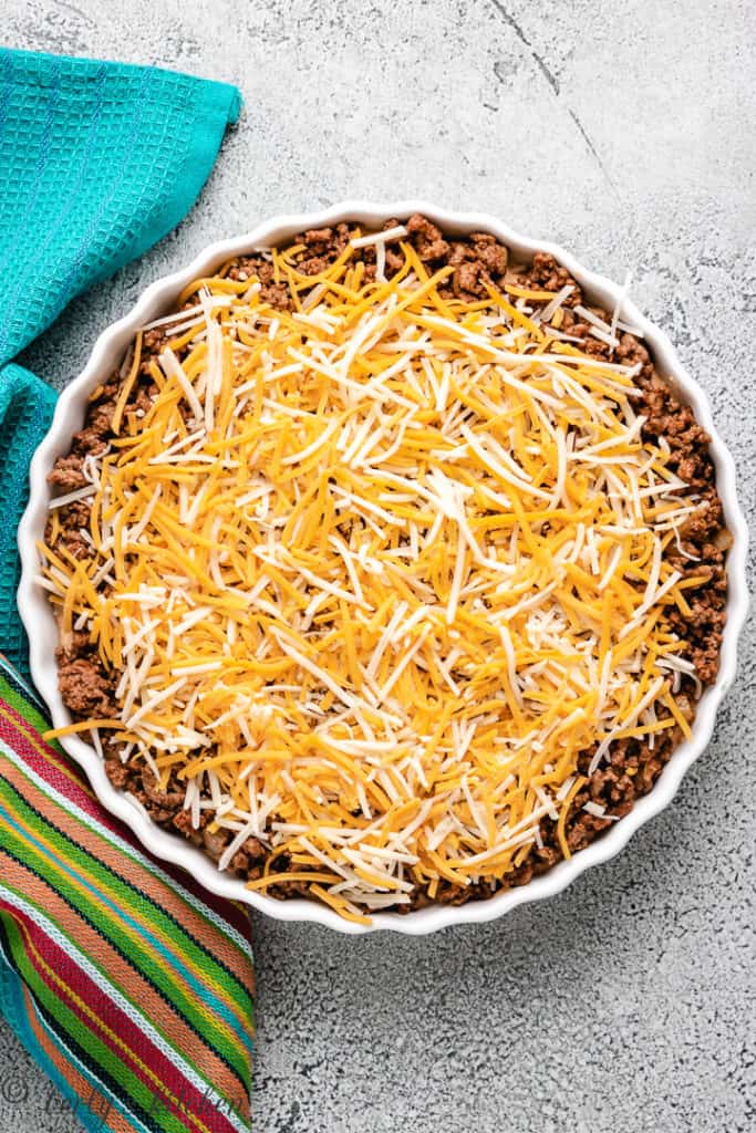 Shredded cheese on top of taco meat in a dish.