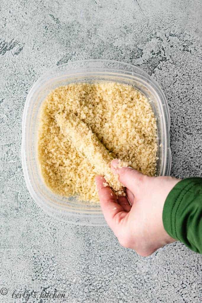 Top down view of a pickle being dipped in panko.