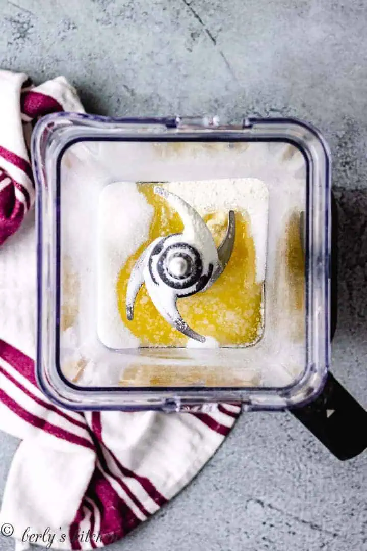 Top down view of dry milk, sugar, and butter in a blender.
