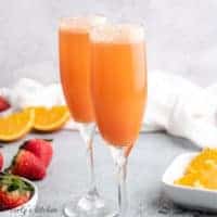 Two long stemmed glasses filled with strawberry mimosas.