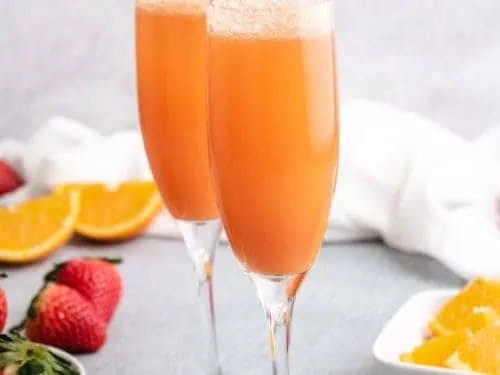 Two long stemmed glasses filled with strawberry mimosas.