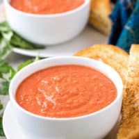 Two bowls tomato basil soup served with grilled cheese sandwiches.