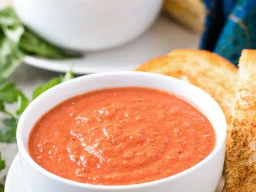 Two bowls tomato basil soup served with grilled cheese sandwiches.