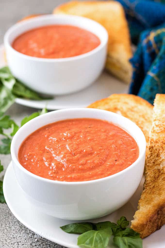 Two bowls tomato basil soup served with grilled cheese sandwiches.