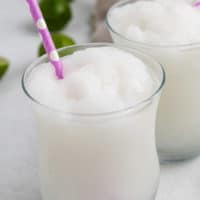 White frozen drink in a glass with a pink straw.