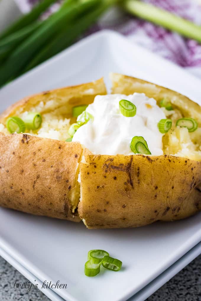 Instant pot baked potatoes on a plate with sour cream and chives.