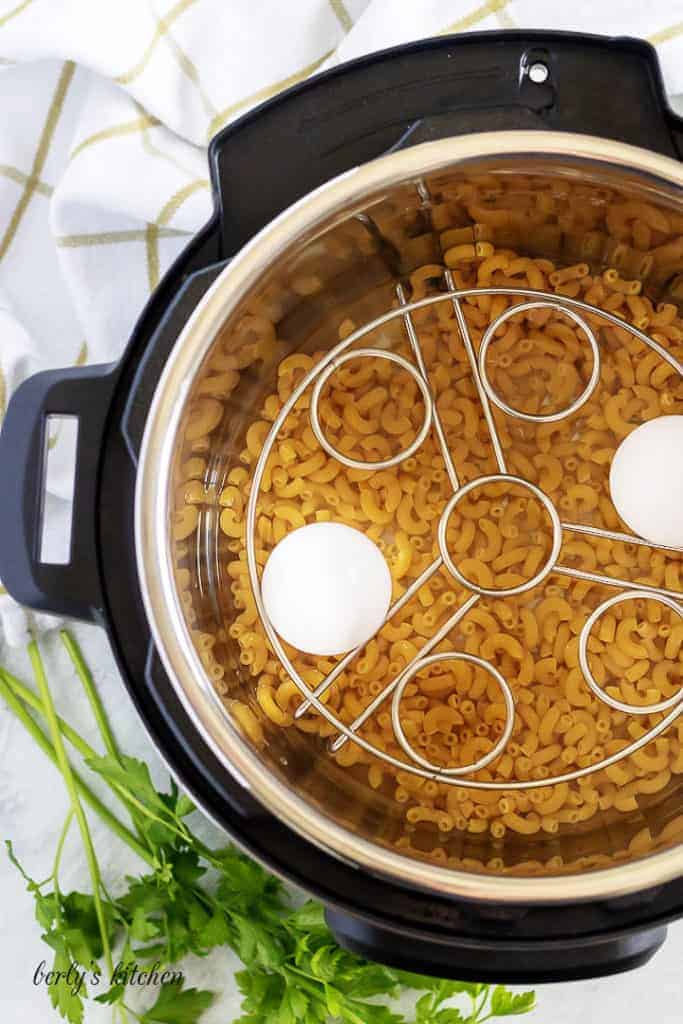 Dry macaroni, a trivet and two eggs, sitting in the pressure cooker.