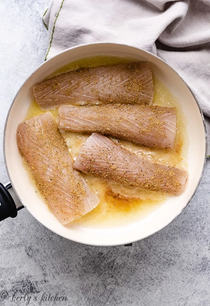 Mahi mahi fillets cooking in a skillet with butter and olive oil.