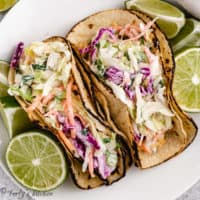 Top down view of fish tacos on a plate with fresh lime halves.
