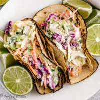 Top down view of fish tacos on a plate with fresh lime halves.