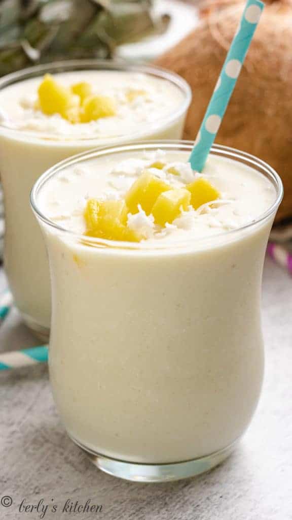 Two glasses with a tropical smoothie and blue and white straw.