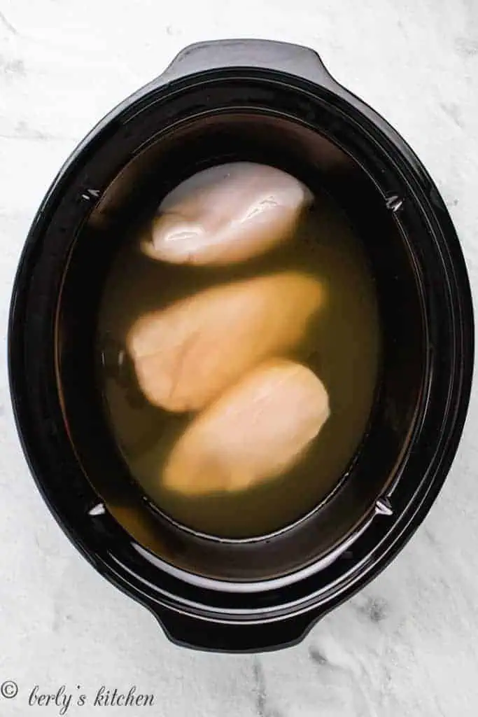 Chicken breasts and broth in a slow cooker.