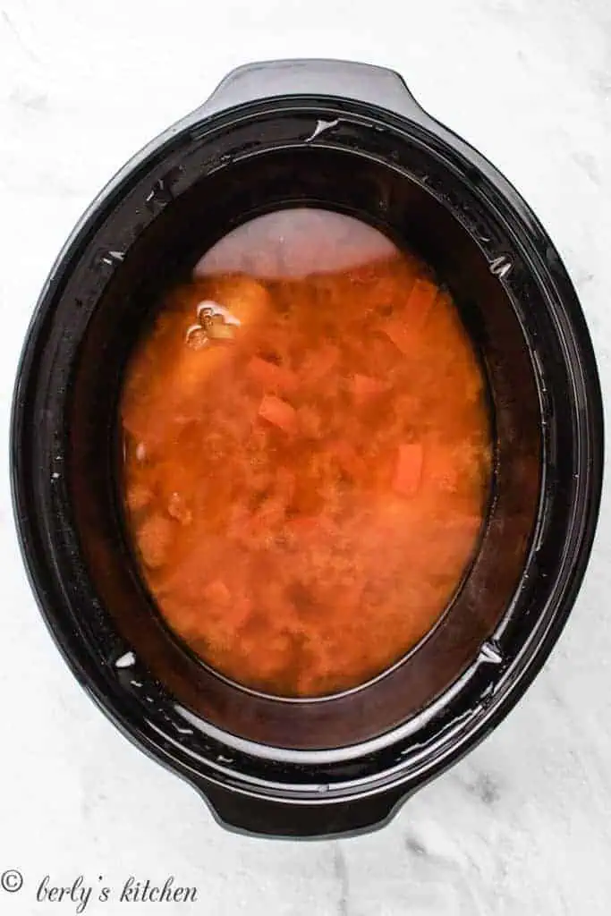 Top down view of a slow cooker with cooked chicken breasts in broth.