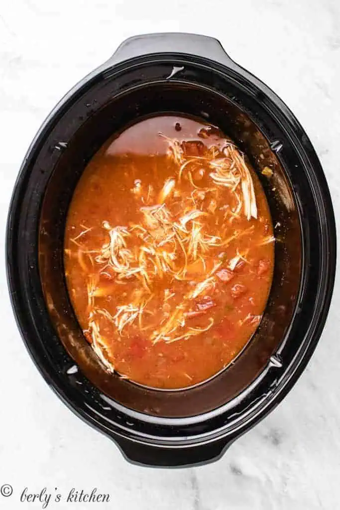 Top down view of shredded chicken in broth in a slow cooker.
