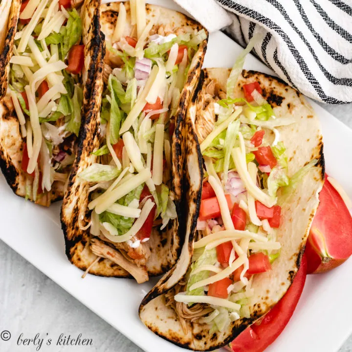 Chicken tacos in a row on a white serving platter.