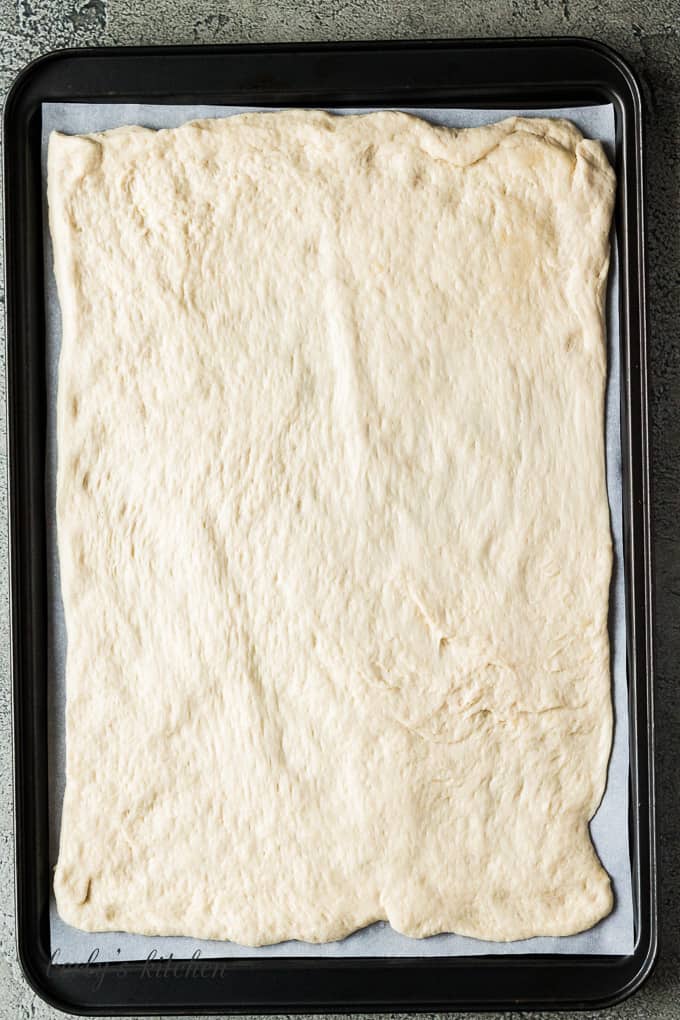 Pizza dough rolled out on a baking sheet.