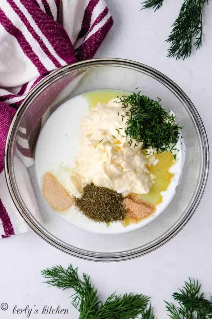 Top down view of ingredients for dill dressing in a glass bowl.