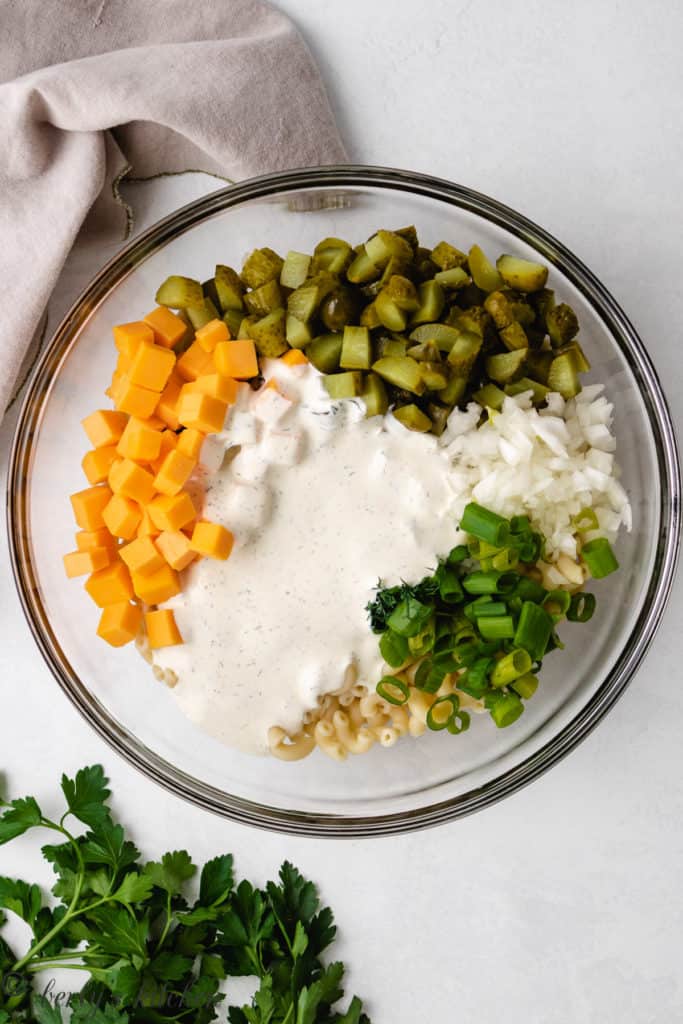 Top down view of ingredients of dill pickle pasta salad in a bowl.