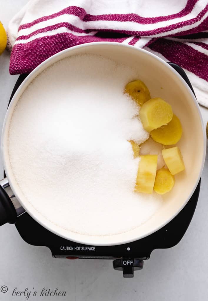Top down view of sugar and ginger root in a saucepan.