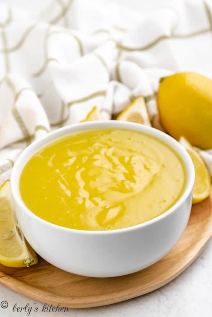 White bowl of lemon filling next to fresh, whole lemons.