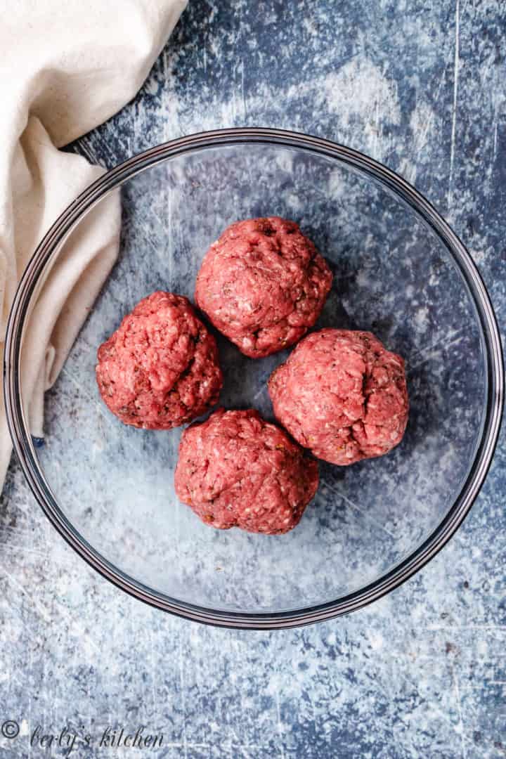 Top down view of 4 portions of ground beef in a bowl.
