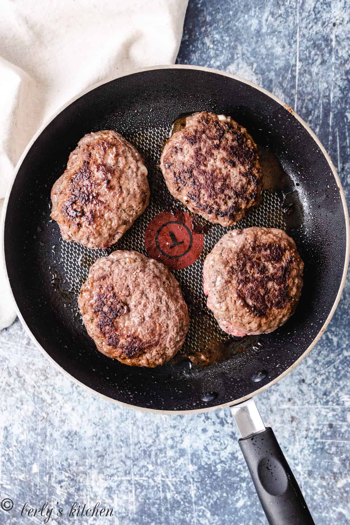 Top down photo of 4 burgers cooking in a skillet.