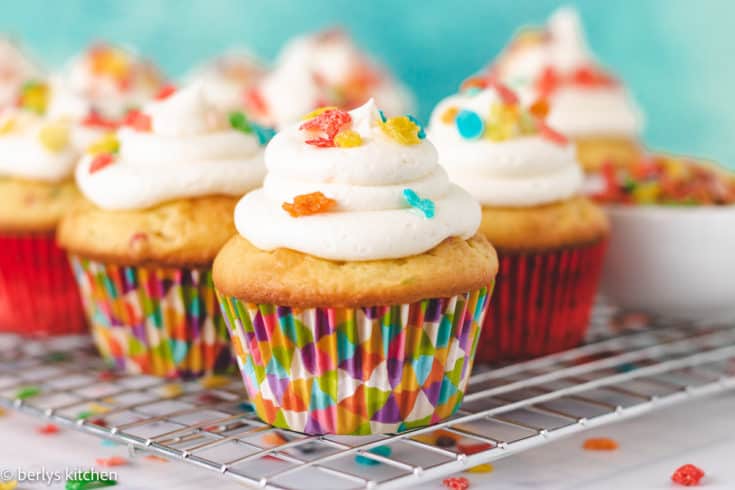 Several cupcakes topped with colorful cereal.