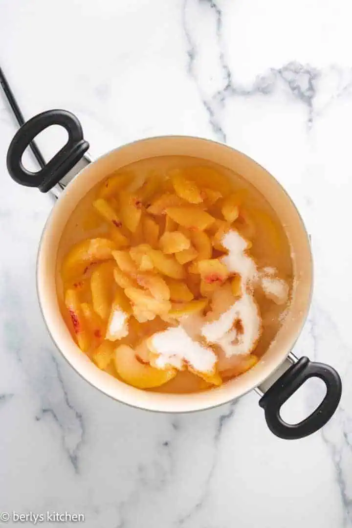 Top down view of peaches and sugar in a pan.