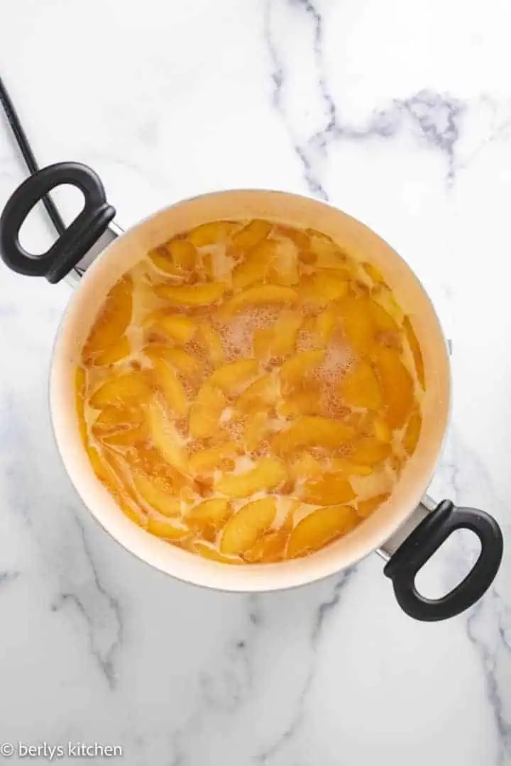 Top down view of peaches cooking in a saucepan.