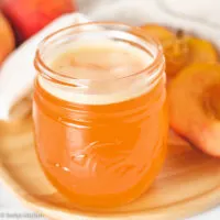 Peach syrup in a jar next to fresh peaches.