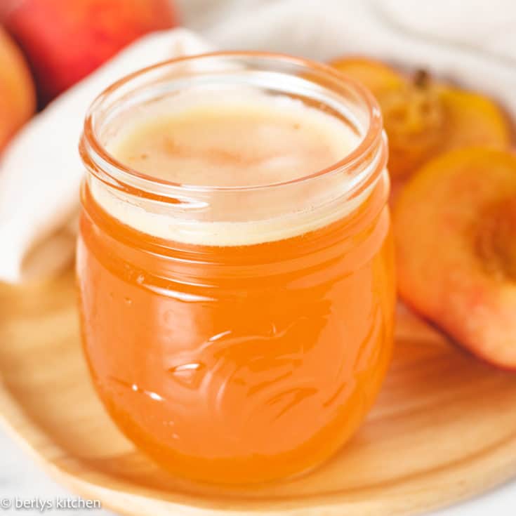 Peach syrup in a jar next to fresh peaches.