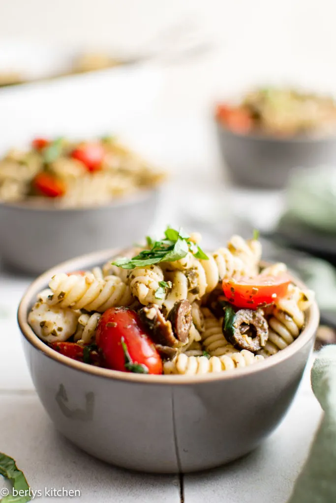 Gray bowl filled with pasta salad with olives and tomatoes.