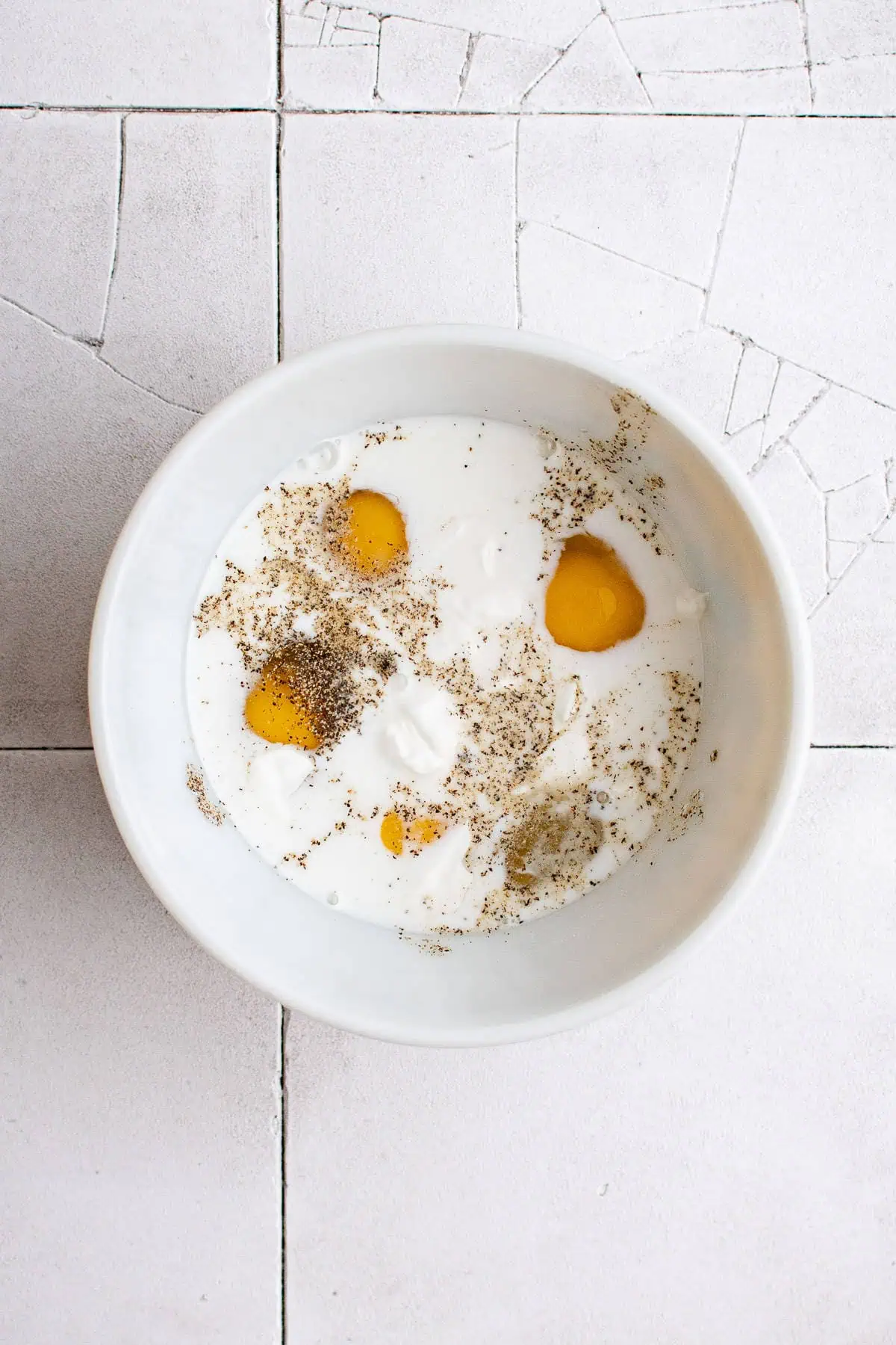 Top down view of eggs, milk, salt and pepper in a dish.